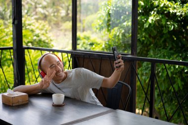 Kel bir Asyalı çocuk, bir kafede takılırken telefonundan bir video mesajı aldığında mutlu görünüyor..