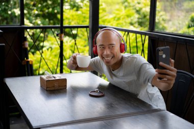 Kel bir Asyalı çocuk, bir kafede takılırken bir fincan kahvenin tadını çıkarırken akıllı telefonundan bir video mesajı aldığında mutlu görünüyor..