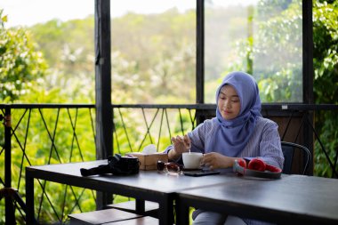 Bir kafede yalnız başına kahve içen tesettürlü genç Asyalı kadın..