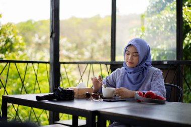 Bir kafede yalnız başına kahve içen tesettürlü genç Asyalı kadın..