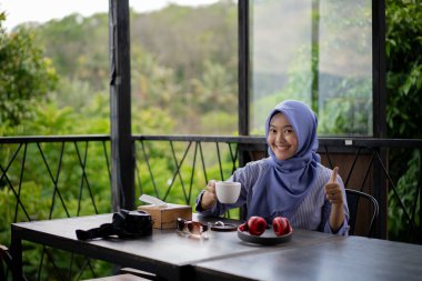 Bir kafede yalnız başına kahve içen tesettürlü genç Asyalı kadın..