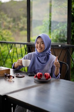 Bir kafede yalnız başına kahve içen tesettürlü genç Asyalı kadın..