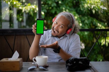 Restoranda ya da kafede oturan mutlu Asyalı adam telefonu açık yeşil ekranlı gösteriyor. Restoran, yemek siparişi başvurusu..