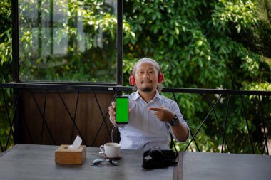 happy asian man sitting in restaurant or cafe using showing phone with blank green screen. Restaurant, food order application. clipart