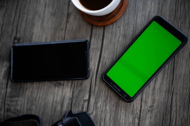 green screen phone on table with coffee and headphones. A flat lay of a mobile phone with blank green screen on a marble table background with a cup of latte. High Angle View. Concept workplace. clipart