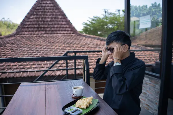 Genç bir adam açık kahve dükkanında ya da kafede kahve içiyor.