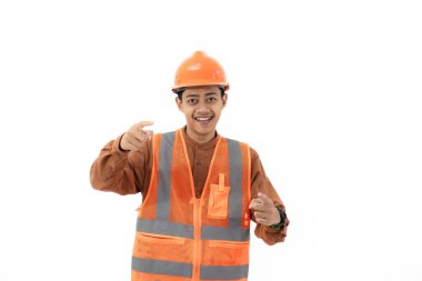 Endonezyalı genç inşaat işçisi tam güvenlik teçhizatıyla kameraya, endüstriyel ve inşaat konseptine, izole edilmiş beyaz arka plana başparmağıyla güvenle duruyor..