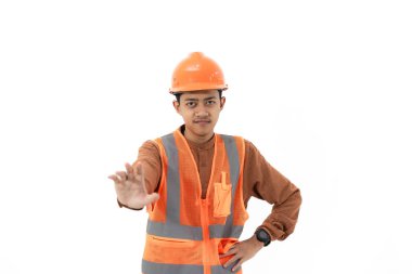 Endonezyalı genç inşaat işçisi, güvenlik teçhizatıyla kameraya, inşaata ve sanayi konseptine işaret ederek beyaz arka planda izole bir şekilde el hareketi yapıyor..