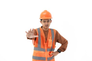 Endonezyalı genç inşaat işçisi, güvenlik teçhizatıyla kameraya, inşaata ve sanayi konseptine işaret ederek beyaz arka planda izole bir şekilde el hareketi yapıyor..