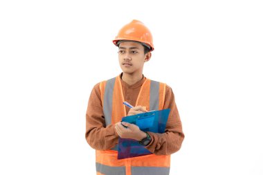 Endonezyalı genç erkek inşaat işçisi beyaz arka planda izole edilmiş bir pano, inşaat ve endüstri konsepti hakkında bir rapor dolduruyor..