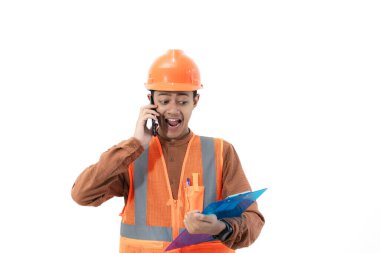 Endonezyalı genç erkek inşaat işçisi, beyaz arka planda izole edilmiş bir pano, inşaat ve sanayi konseptini elinde tutarken iş arkadaşıyla sesli çağrıda bulunuyor..