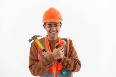 Çekiç ve matkap taşıyan Endonezyalı genç erkek inşaat işçisi beyaz arka planda izole edilmiş kamera, inşaat ve sanayi konseptine bakarken.