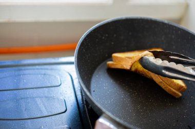 Bir kadının elleri kızartma tavasında sandviç kızartıyor.