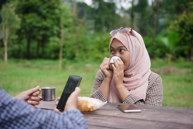 Genç Endonezyalı tesettürlü kadın arkadaşlarıyla piknik yaparken sade kahvenin tadını çıkarıyor..