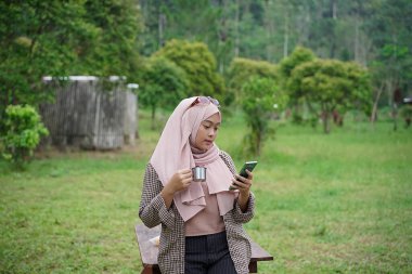 Genç Endonezyalı kadın tesettüre binmiş, rahatlatıcı doğal atmosferin tadını çıkarırken bir fincan sade kahvenin tadını çıkarıyor, şehrin koşuşturma ve telaşından uzakta, seyahat konseptinden uzakta..