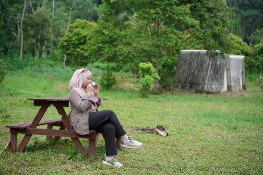 Genç Endonezyalı kadın tesettüre binmiş, rahatlatıcı doğal atmosferin tadını çıkarırken bir fincan sade kahvenin tadını çıkarıyor, şehrin koşuşturma ve telaşından uzakta, seyahat konseptinden uzakta..