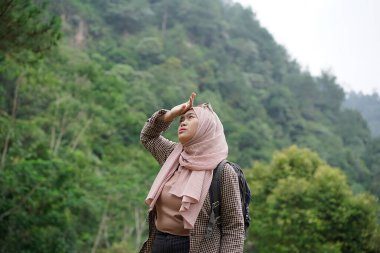 Endonezyalı genç bayan gezgin tesettür giyiyor. Doğada seyahat ederken yorgun görünüyor. Seyahat konsepti..