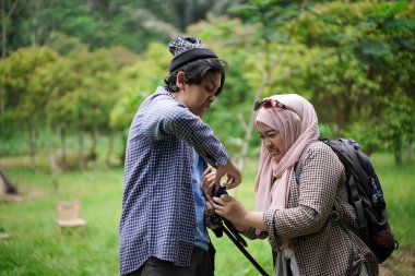 Endonezyalı genç bir adam, Endonezyalı genç bir kadının doğada yürürken ve seyahat konseptinde video kayıt cihazları hazırlamasına yardım ediyor..