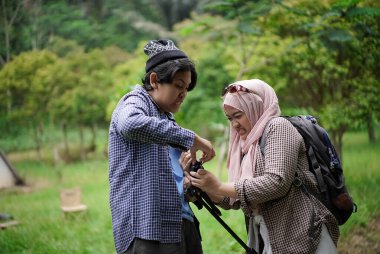 Endonezyalı genç bir adam, Endonezyalı genç bir kadının doğada yürürken ve seyahat konseptinde video kayıt cihazları hazırlamasına yardım ediyor..