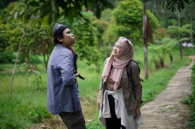 Endonezyalı genç bir adam, Endonezyalı genç bir kadının doğada yürürken ve seyahat konseptinde video kayıt cihazları hazırlamasına yardım ediyor..