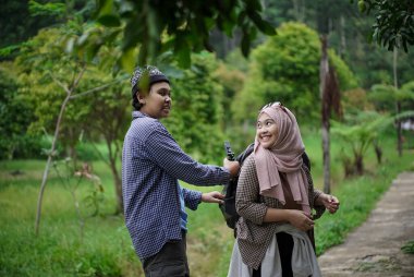 Endonezyalı genç bir adam, Endonezyalı genç bir kadının doğada yürürken ve seyahat konseptinde video kayıt cihazları hazırlamasına yardım ediyor..