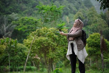 Endonezyalı genç bir kadın doğal manzaranın, doğal atmosferin ve seyahat konseptinin tadını çıkarırken doğada yürürken tesettür takıyor..