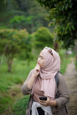 Kafası karışık genç Endonezyalı kadın doğada yürürken yön arıyor, seyahat konsepti.