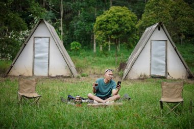 Kel kafalı Endonezyalı bir adam orman kulübesinde kalırken bir fincan kahvenin tadını çıkarıyor, seyahat konsepti..