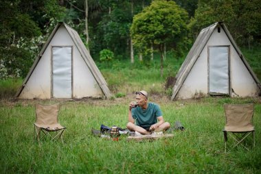 Kel kafalı Endonezyalı bir adam orman kulübesinde kalırken bir fincan kahvenin tadını çıkarıyor, seyahat konsepti..