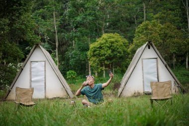 Kel kafalı Endonezyalı bir adam orman kulübesinde kalırken bir fincan kahvenin tadını çıkarıyor, seyahat konsepti..