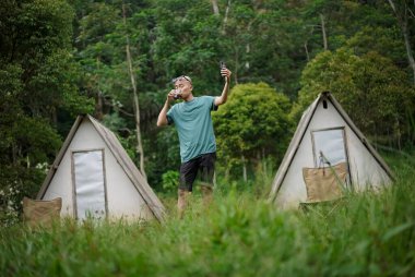 Kel kafalı Endonezyalı bir adam orman kulübesinde kalırken bir fincan kahvenin tadını çıkarıyor, seyahat konsepti..