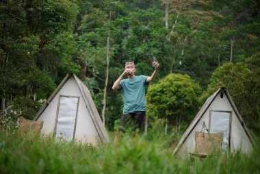 Kel kafalı Endonezyalı bir adam orman kulübesinde kalırken bir fincan kahvenin tadını çıkarıyor, seyahat konsepti..