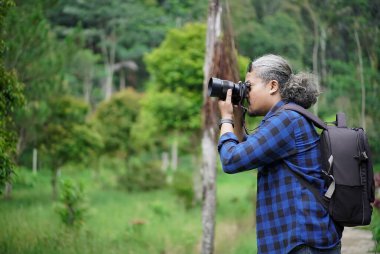 Erkek profesyonel fotoğrafçı ormanda yürürken doğal manzaranın fotoğraflarını çekiyor, seyahat konsepti.