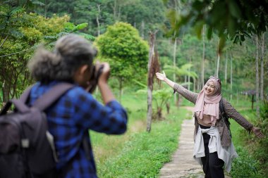 Profesyonel fotoğrafçı, Endonezyalı genç bir kadın modelin başörtüsü içinde fotoğraf çekiyor. Doğada seyahat ederken poz veriyor. Seyahat kavramı..