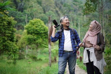 Kıvırcık saçlı Endonezyalı erkek ve genç Endonezyalı kadın doğal manzaranın tadını çıkarırken ormandaki doğal manzaranın, seyahat konseptinin fotoğraflarını çekiyorlar.