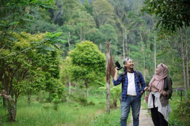 Kıvırcık saçlı Endonezyalı erkek ve genç Endonezyalı kadın doğal manzaranın tadını çıkarırken ormandaki doğal manzaranın, seyahat konseptinin fotoğraflarını çekiyorlar.