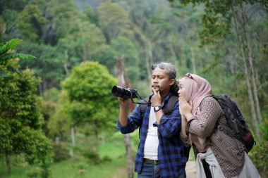 Kıvırcık saçlı Endonezyalı erkek ve genç Endonezyalı kadın doğal manzaranın tadını çıkarırken ormandaki doğal manzaranın, seyahat konseptinin fotoğraflarını çekiyorlar.