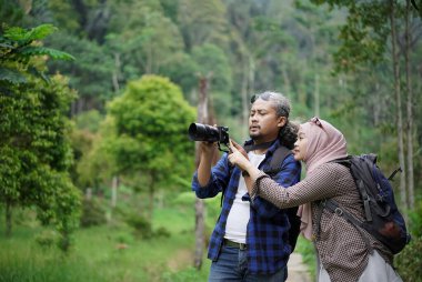 Kıvırcık saçlı Endonezyalı erkek ve genç Endonezyalı kadın doğal manzaranın tadını çıkarırken ormandaki doğal manzaranın, seyahat konseptinin fotoğraflarını çekiyorlar.