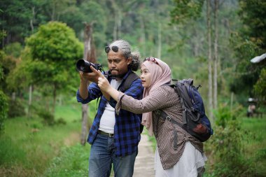 Kıvırcık saçlı Endonezyalı erkek ve genç Endonezyalı kadın doğal manzaranın tadını çıkarırken ormandaki doğal manzaranın, seyahat konseptinin fotoğraflarını çekiyorlar.