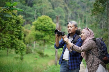 Kıvırcık saçlı Endonezyalı erkek ve genç Endonezyalı kadın doğal manzaranın tadını çıkarırken ormandaki doğal manzaranın, seyahat konseptinin fotoğraflarını çekiyorlar.