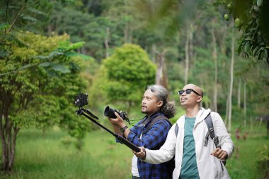 İki Endonezyalı erkek gezgin doğada yürürken video çekerken manzaranın fotoğraflarını çekiyorlar, seyahat konsepti.