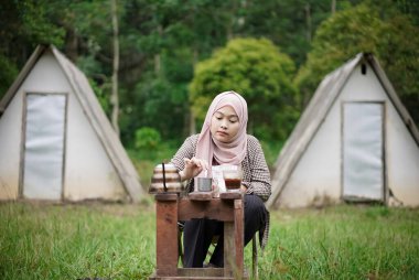 Endonezyalı genç bir kadın orman kulübesinde kamp yaparken kahve yapıyor, doğanın güzelliğinin ve atmosferinin tadını çıkarıyor, seyahat kavramının..