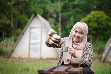 Endonezyalı genç bir kadın orman kulübesinde kamp yaparken kahve yapıyor, doğanın güzelliğinin ve atmosferinin tadını çıkarıyor, seyahat kavramının..