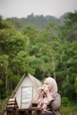 Endonezyalı genç kadın bir fincan sade kahvenin keyfini çıkarırken doğanın güzelliğinin ve rahatlatıcı atmosferinin tadını çıkarıyor. Seyahat kavramı..