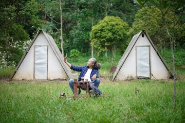 Bir orman kulübesinde kamp yaparken görüntülü konuşan kıvırcık saçlı Endonezyalı. Seyahat kavramı..
