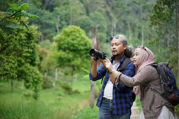 Kıvırcık saçlı Endonezyalı erkek ve genç Endonezyalı kadın doğal manzaranın tadını çıkarırken ormandaki doğal manzaranın, seyahat konseptinin fotoğraflarını çekiyorlar.