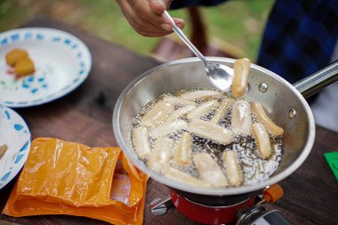 Endonezyalı erkekler orman kulübesinde kamp yaparken mini sosis kızartırlar, hazır yemekler, seyahat konsepti..