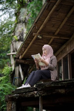 Endonezyalı genç bir kadın orman kulübesinde doğanın tadını çıkarırken kitap okuyor. Seyahat kavramı..