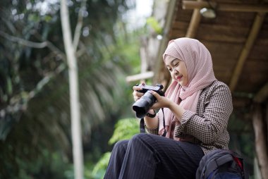 Endonezyalı genç kadın orman kulübesinden doğa manzarası fotoğrafı çekiyor, seyahat konsepti.