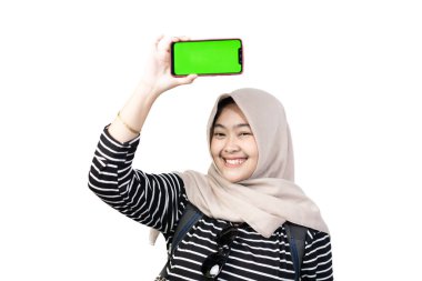 Genç Endonezyalı kadın tesettürcü güvenli bir şekilde kameraya cep telefonu ekranını gösteriyor seyahat ederken, seyahat konsepti taşırken, beyaz arka planda izole edilmiş.